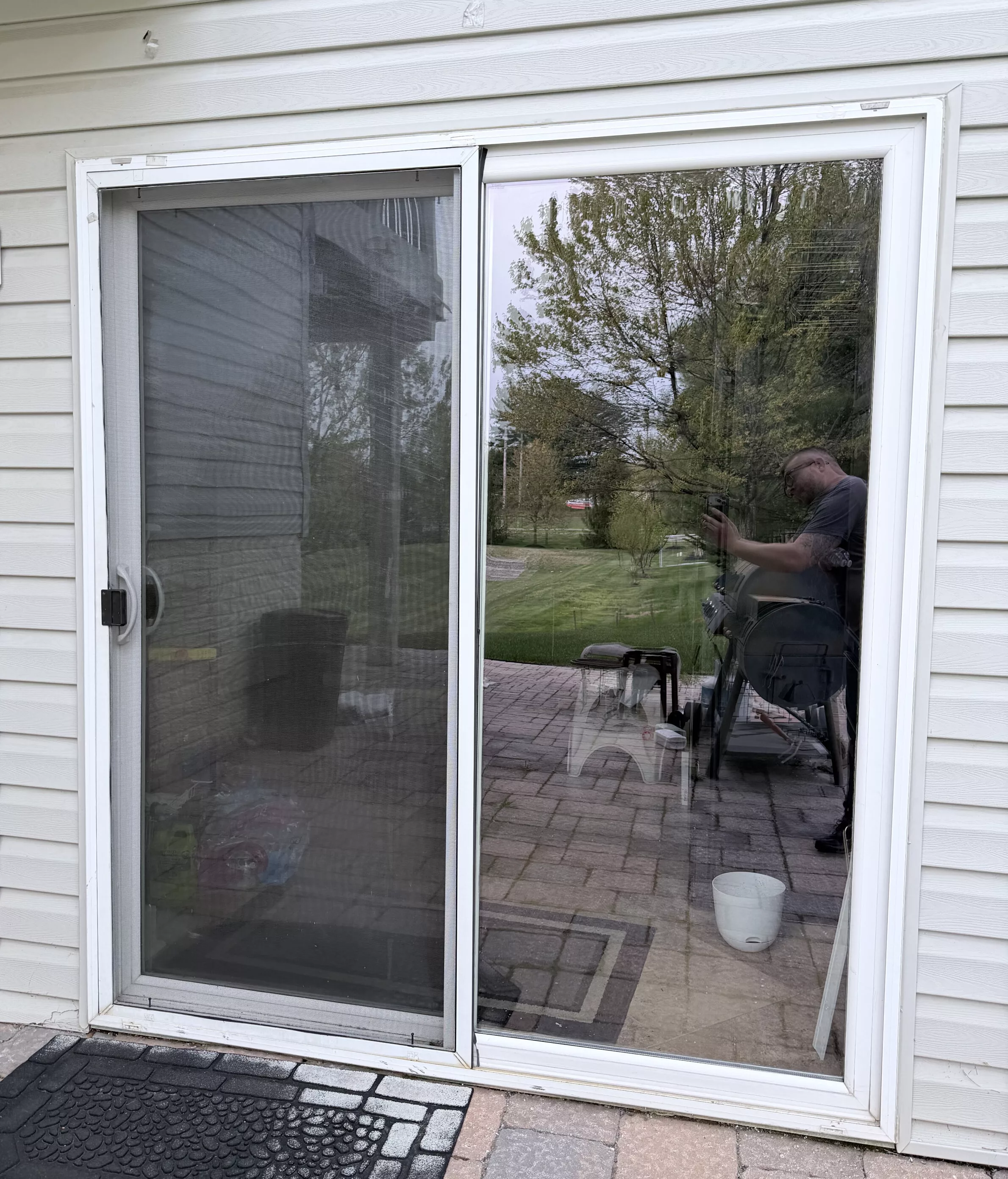Exterior view of a sliding glass door with white siding and a doormat
