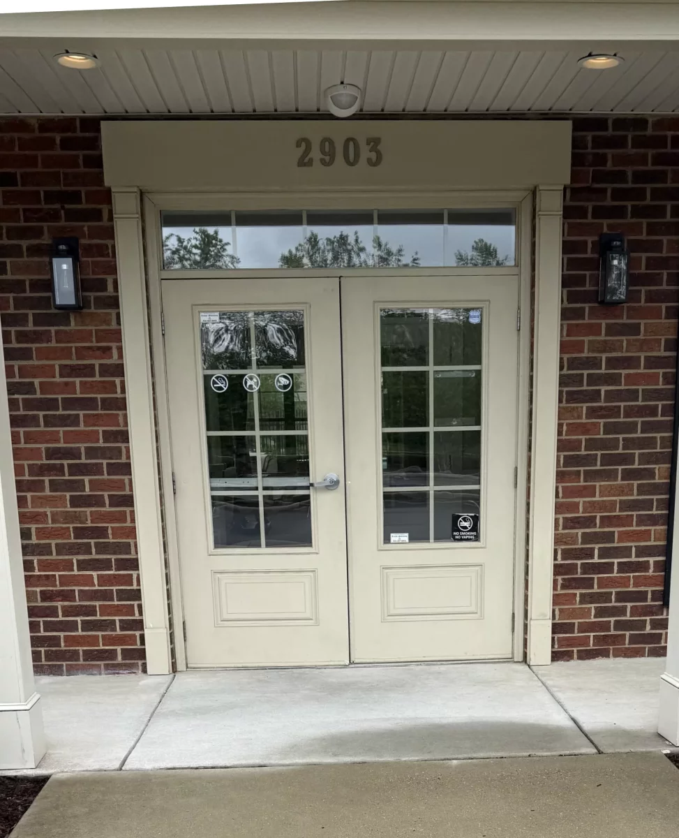 Double glass entry doors with brick facade and concrete walkway