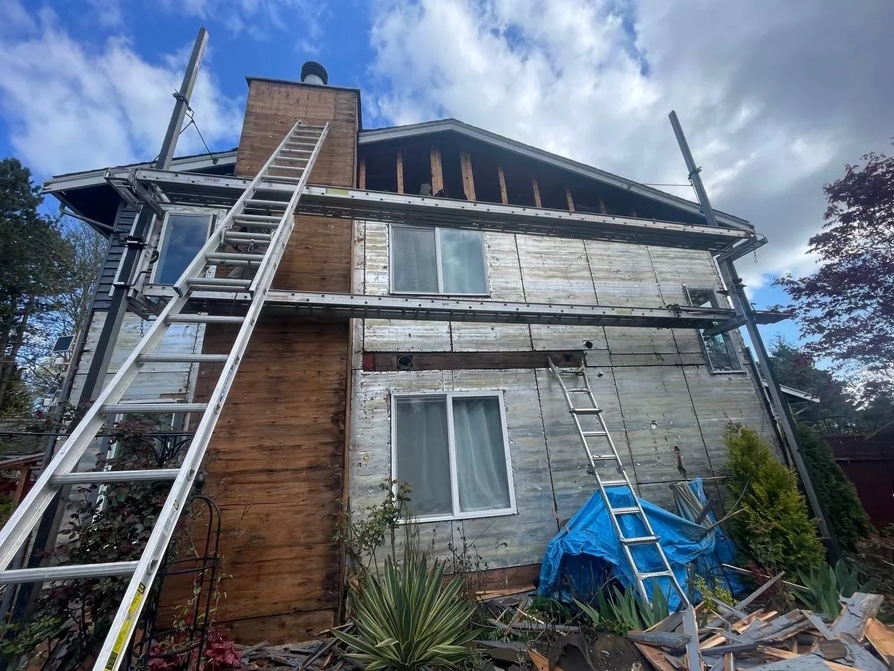 Side of Everett home wrapped in Tyvek weather barrier during siding replacement, ladders in place